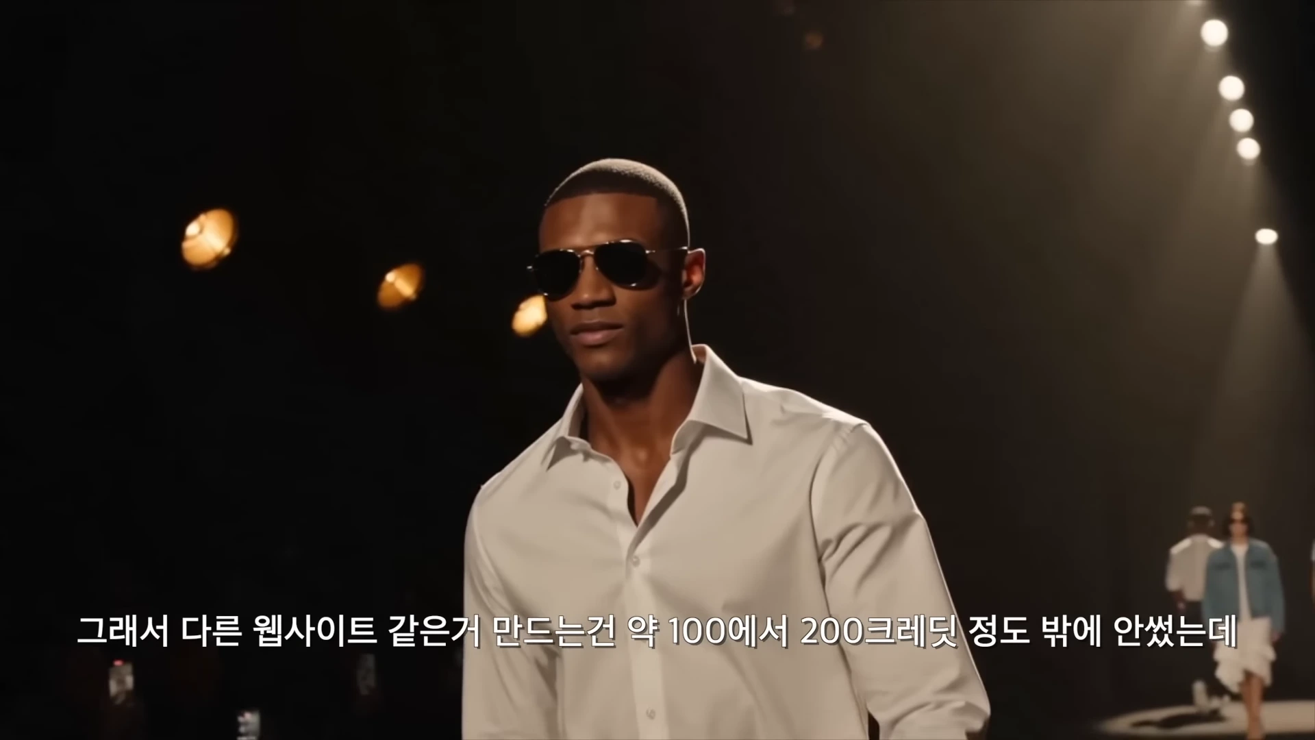 선글라스를 쓴 남성이 흰 셔츠를 입고 어두운 무대 위를 걷는 패션쇼 영상의 한 장면입니다.