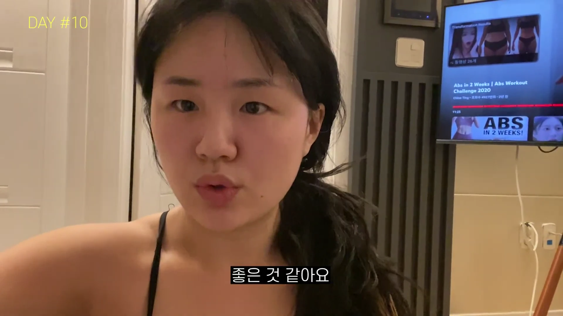 실내에서 운동복을 입은 여성이 카메라를 향해 이야기를 하고 있으며, 배경의 모니터에는 클로이팅의 복근 운동 영상이 재생되고 있다. 왼쪽 상단에는 DAY #10이라는 텍스트가 표시되어 있다.