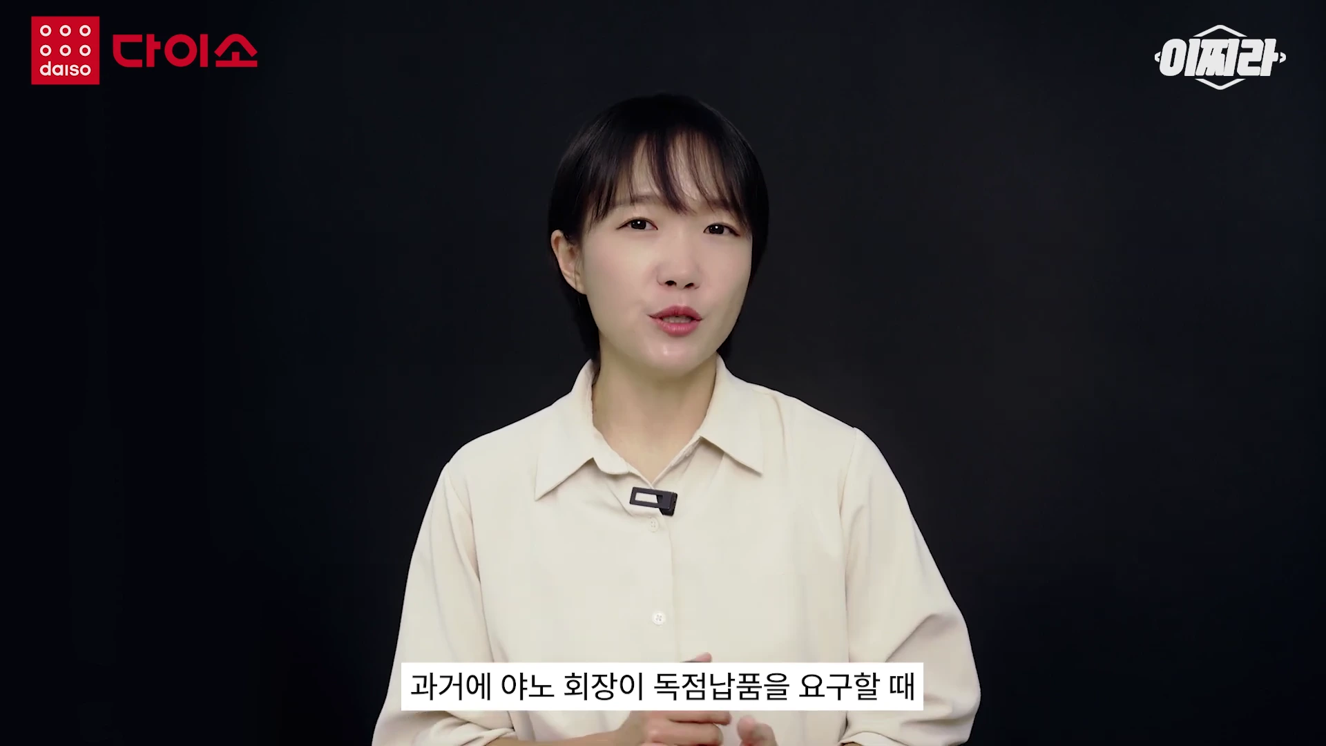 검은색 배경 앞에서 밝은 베이지색 셔츠를 입은 진행자가 정면을 바라보며 이야기하고 있고, 화면 하단에는 '과거에 야노 회장이 독점납품을 요구할 때'라는 자막이 표시되어 있습니다.