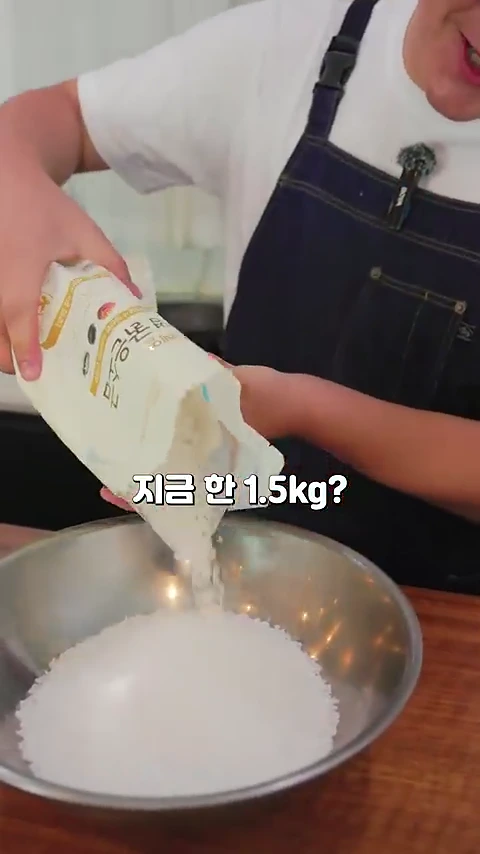 흰색 앞치마를 입은 사람이 커다란 스테인리스 볼에 1.5kg의 소금을 쏟아붓고 있는 모습