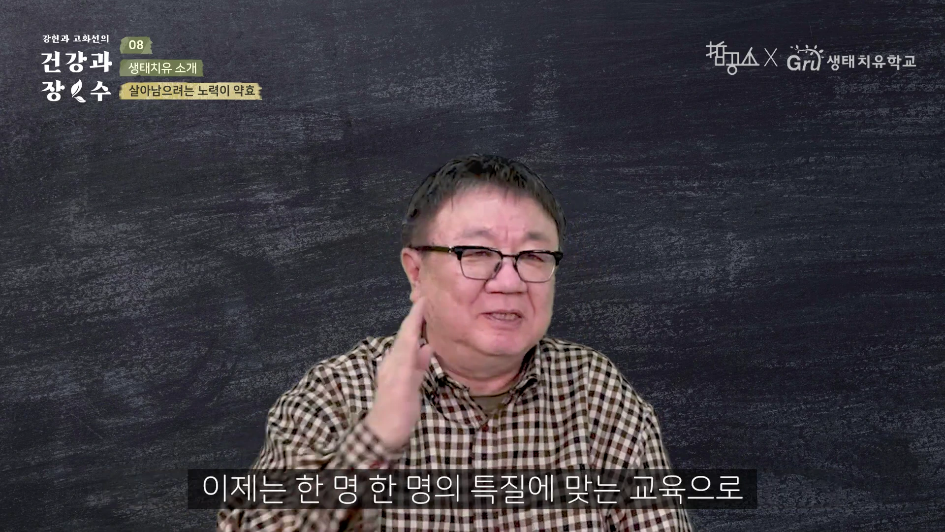 체크무늬 셔츠를 입고 안경을 쓴 중년 남성이 검은 배경 앞에서 손동작을 하며 이야기하는 모습이 담긴 영상 캡처 화면이며, 화면 하단에는 자막이 있고 상단에는 프로그램 제목과 로고가 표시되어 있습니다.