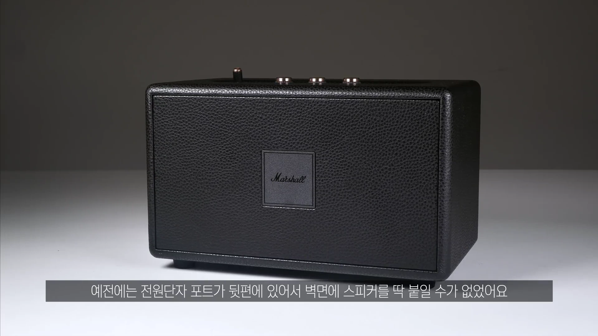 검은색 가죽 질감의 마샬 스피커가 정면을 향해 놓여 있고, 하단에는 한국어 자막이 표시되어 있습니다.