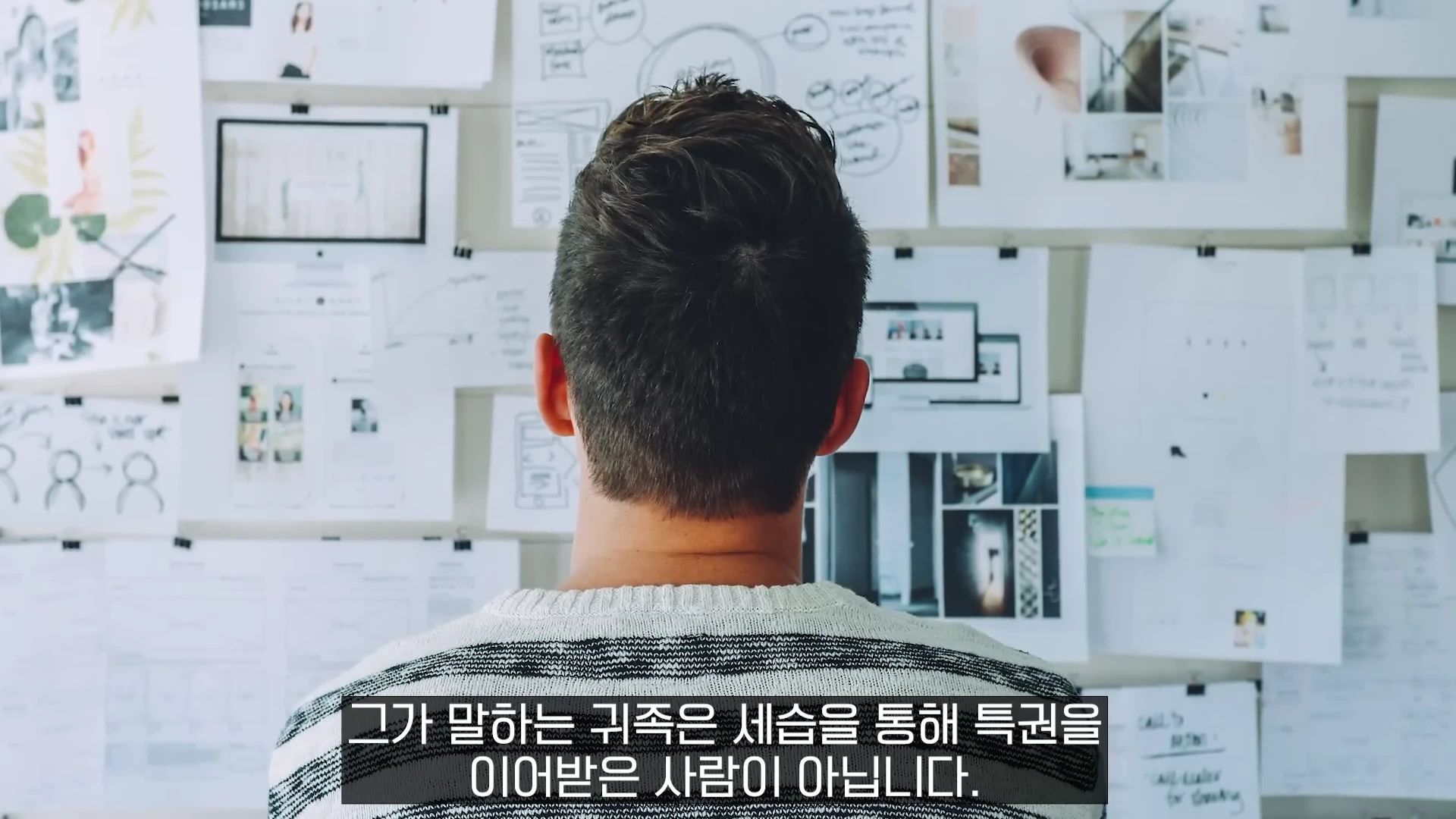 뒷모습의 남자가 아이디어와 다이어그램이 적힌 종이들이 복잡하게 붙어 있는 게시판을 바라보고 있는 모습.