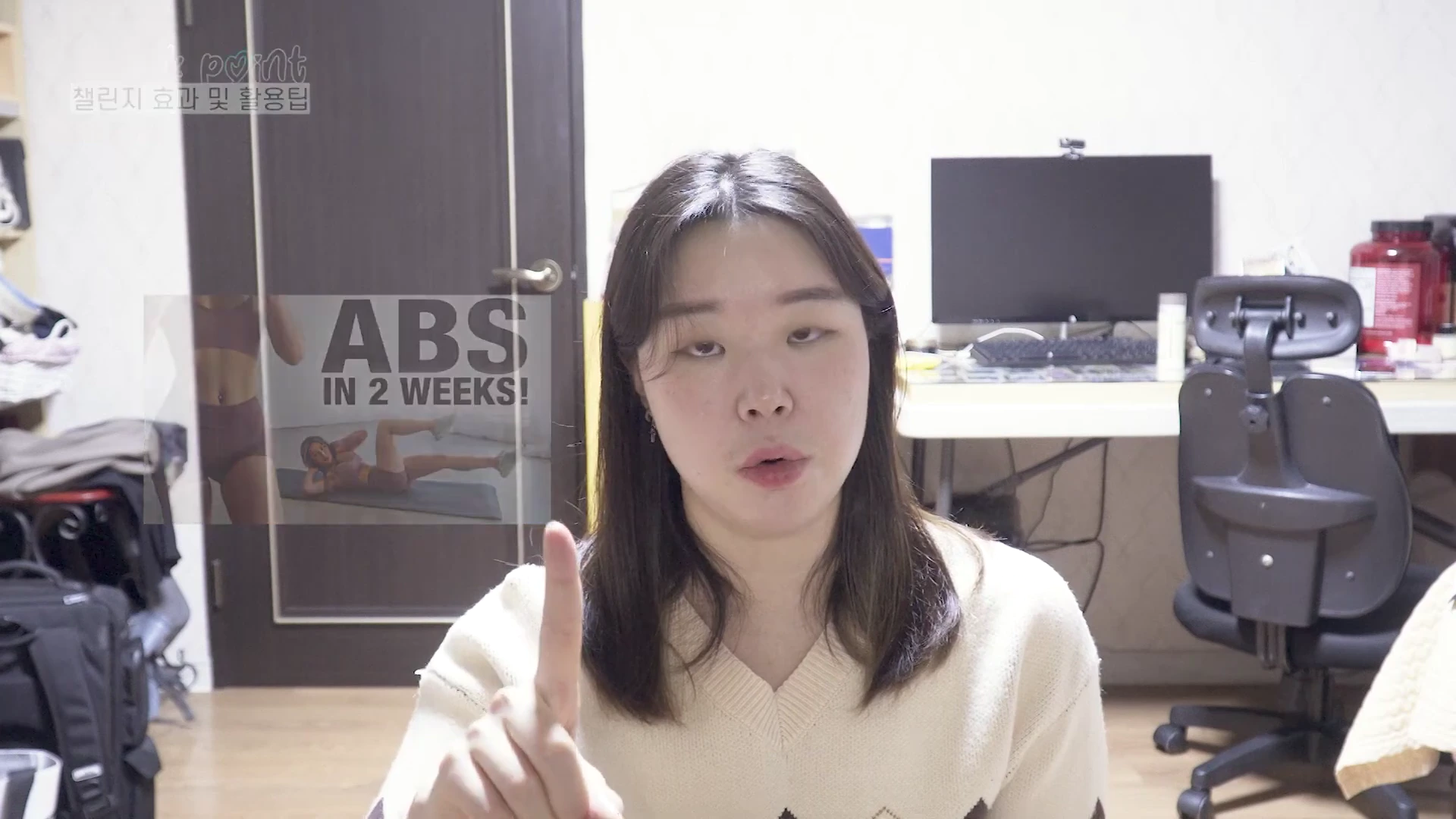 방 안에서 브이넥 니트를 입은 여성이 카메라를 향해 검지 손가락을 세우며 이야기하고 있으며, 화면 왼쪽에는 운동하는 모습이 담긴 작은 영상이 삽입되어 있습니다.