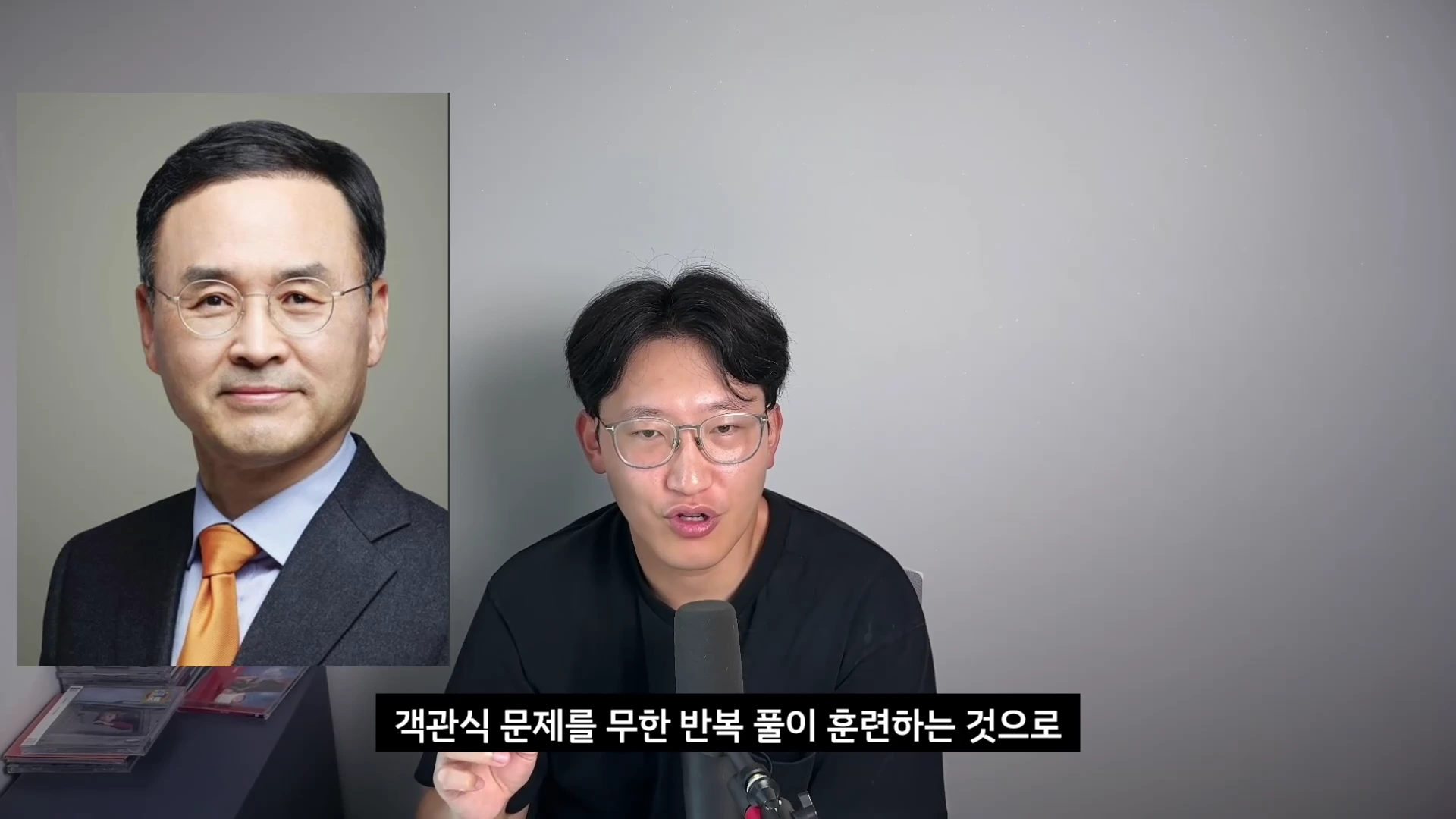 마이크 앞에 앉아 말하는 젊은 남성과 그 옆에 배치된 중년 남성의 정장 사진.
