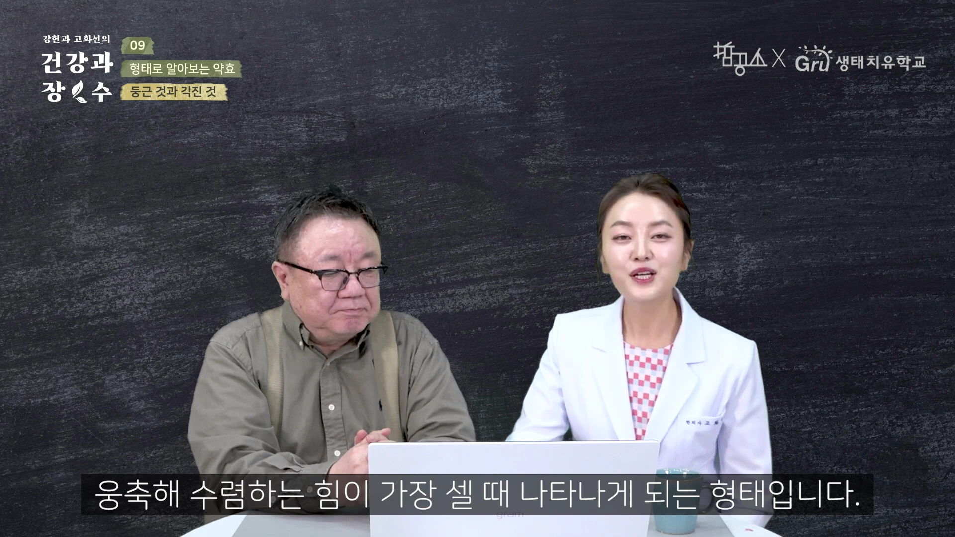 안경을 쓴 중년 남성과 흰색 재킷을 입은 여성이 검은색 칠판을 배경으로 앉아 대담을 나누는 모습이다. 화면 하단에는 흰색 자막이 표시되어 있다.