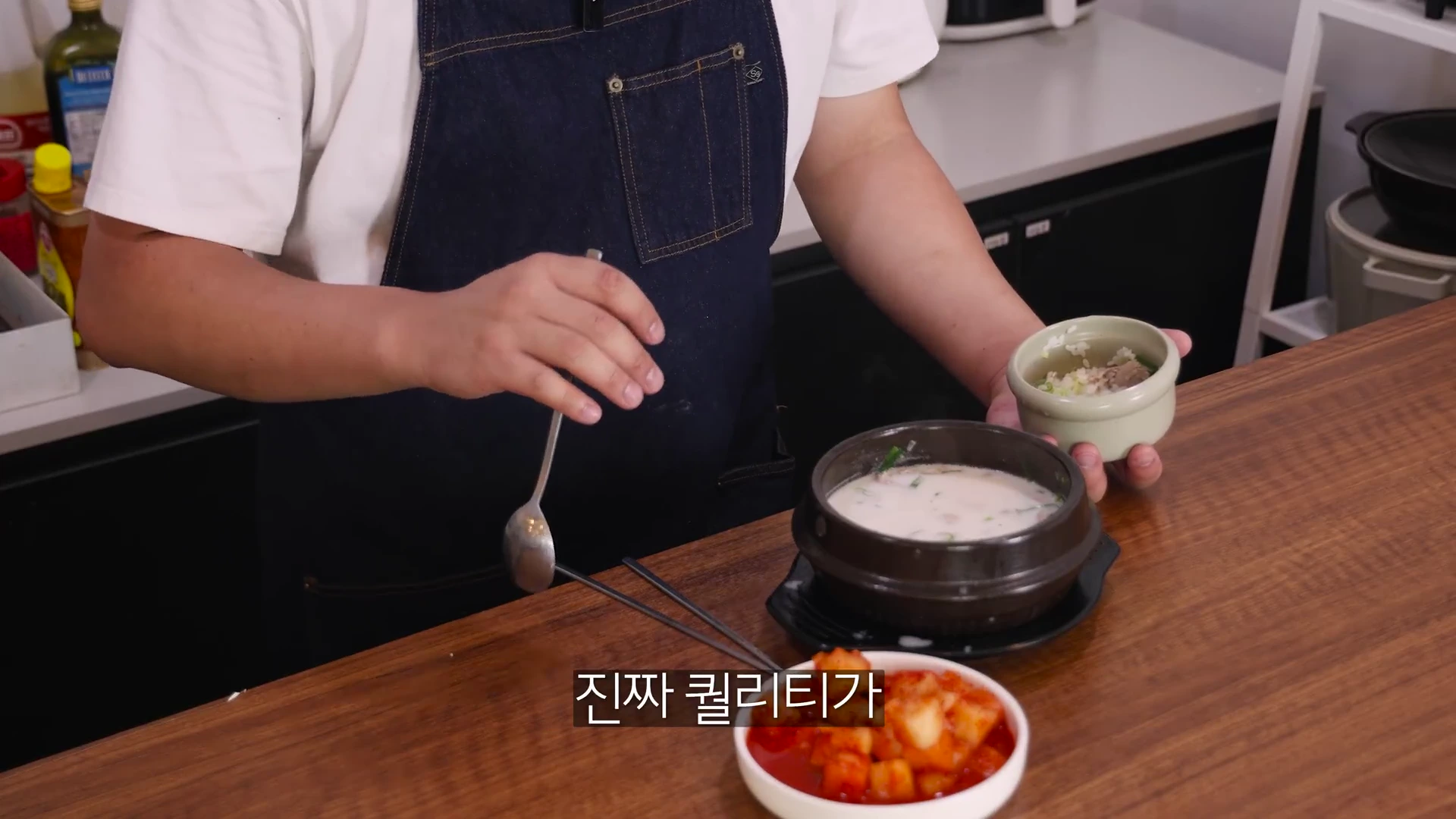 앞치마를 두른 요리사가 뚝배기에 담긴 돼지국밥에 밥을 말 준비를 하고 있는 모습이다.