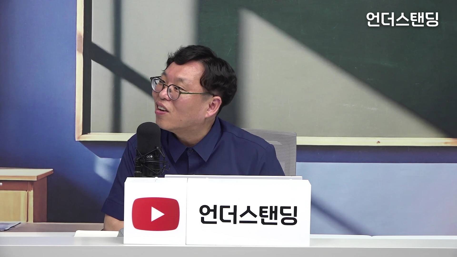 안경을 쓴 남성이 마이크 앞에 앉아 대화를 나누는 스튜디오 토크 화면