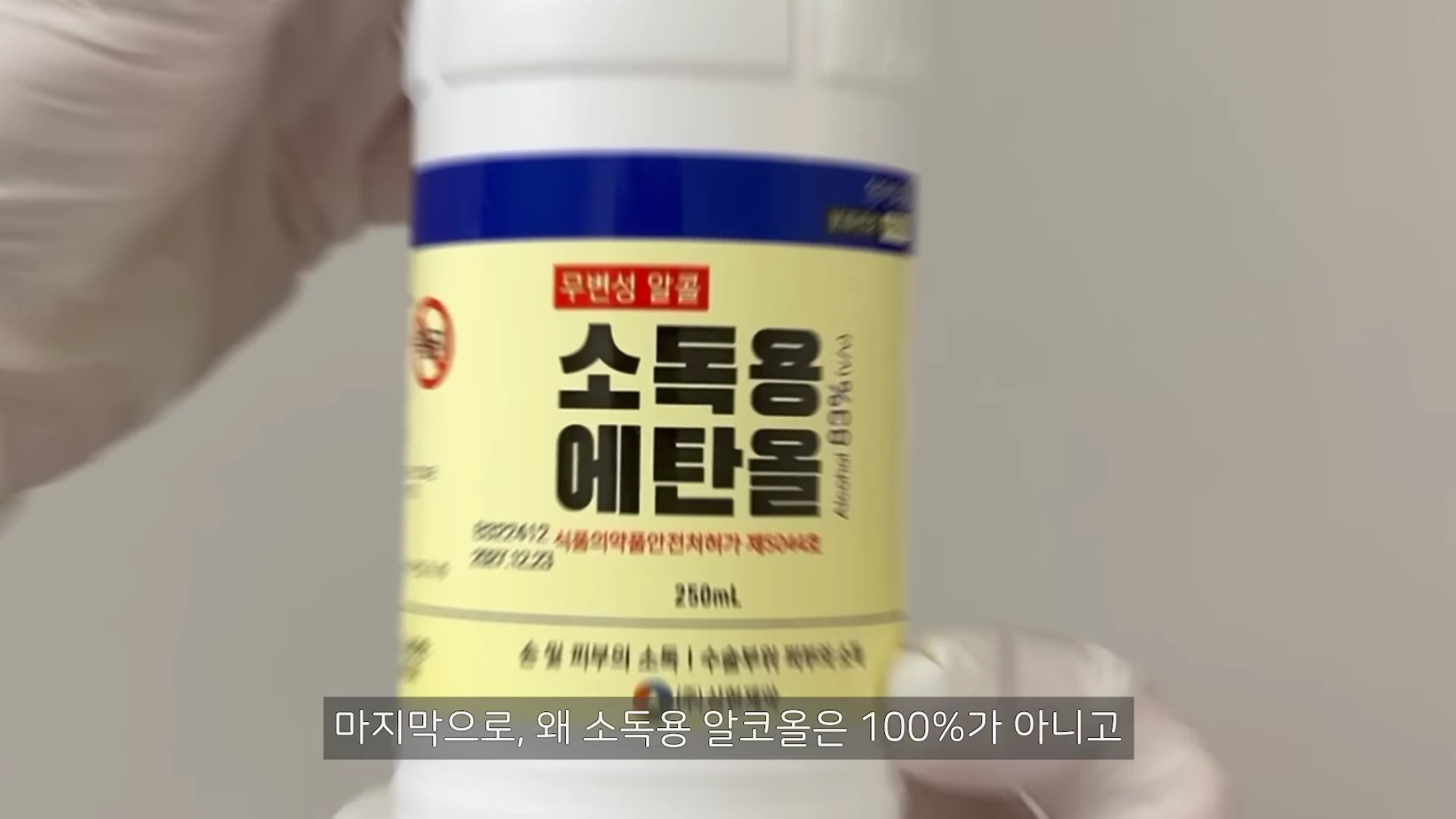 흰색 장갑을 낀 손이 '소독용 에탄올'이라고 적힌 플라스틱 용기를 정면으로 들고 있는 모습.