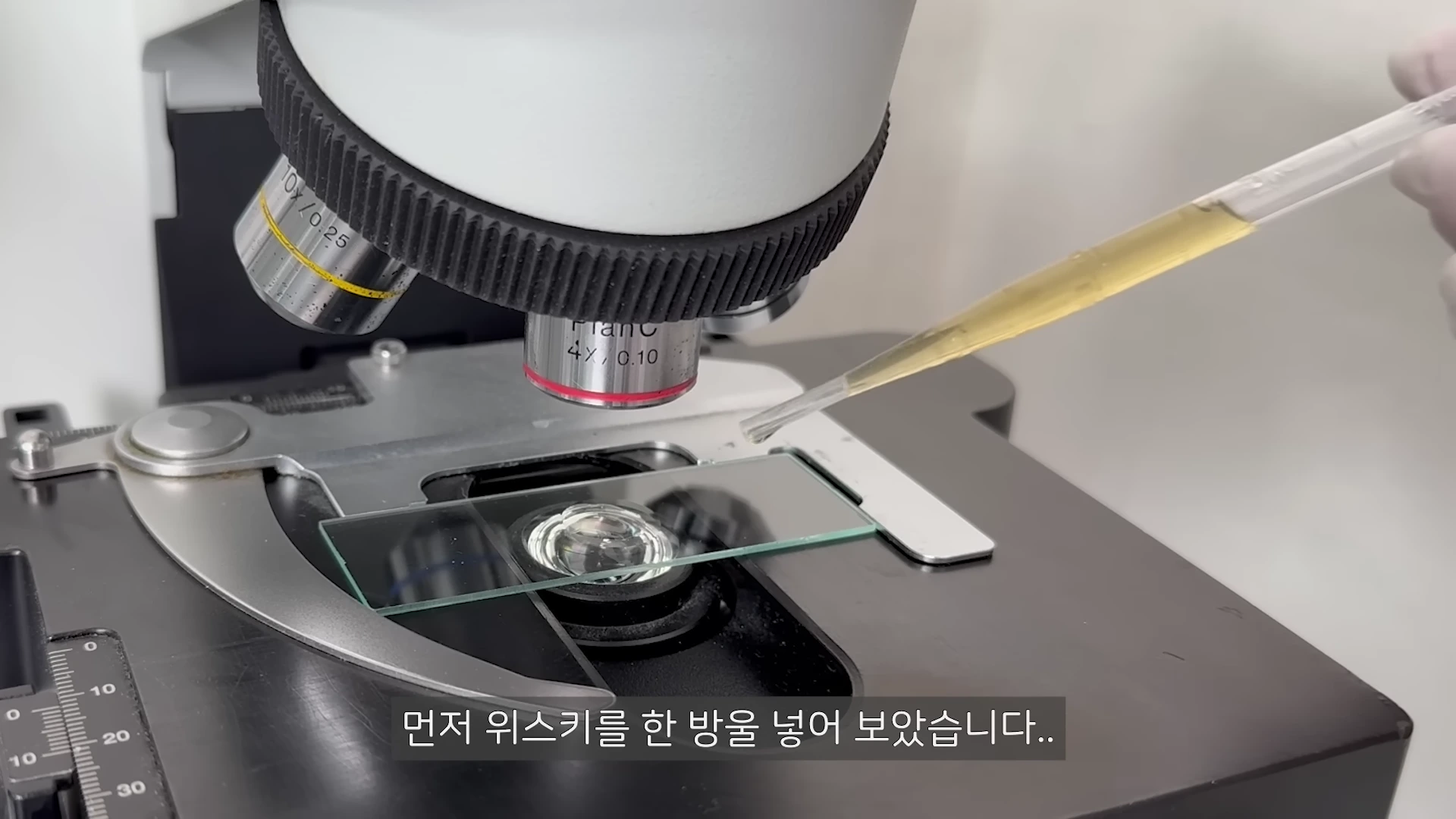 현미경의 재물대 위에 놓인 슬라이드 글라스에 스포이트를 이용해 위스키를 한 방울 떨어뜨리는 모습.