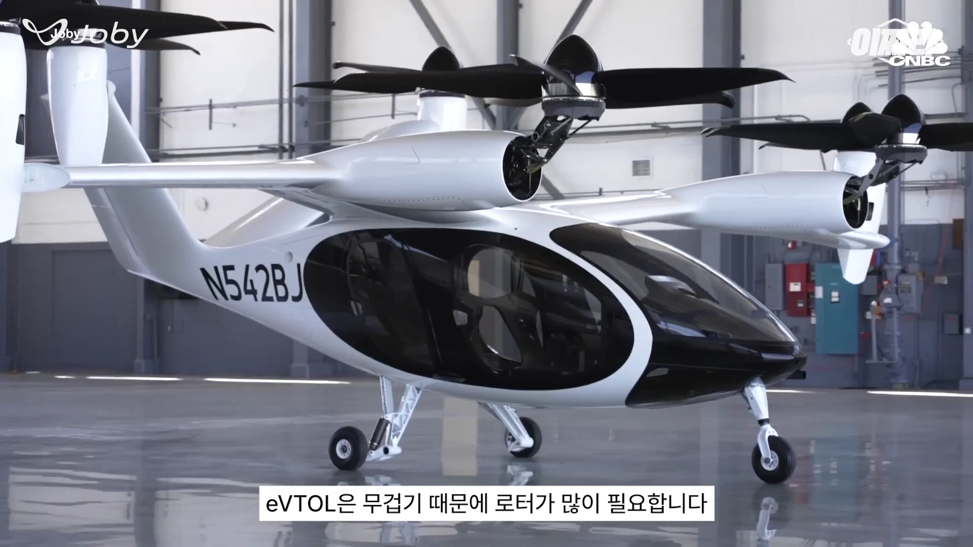 실내 격납고에 주기된 조비 에비에이션의 eVTOL 기체로, 날개 위에 여러 개의 로터가 달려 있고 기체 옆면에는 등록번호가 적혀 있습니다.