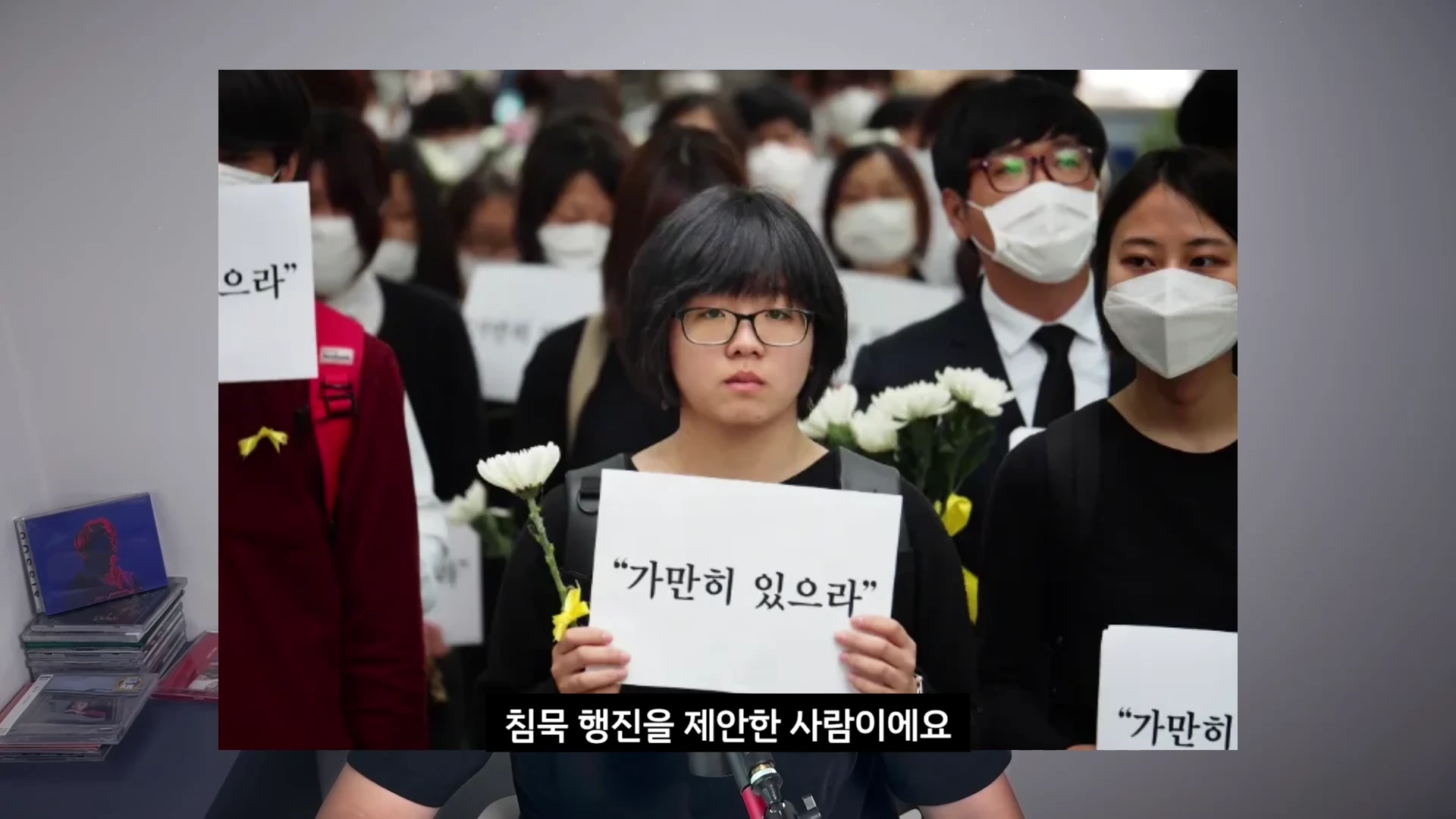 2014년 당시 단발머리에 안경을 쓴 여성이 '가만히 있으라'라고 적힌 피켓을 들고 흰 국화꽃과 함께 침묵 행진에 참여하고 있는 모습이 담긴 영상 캡처 화면.
