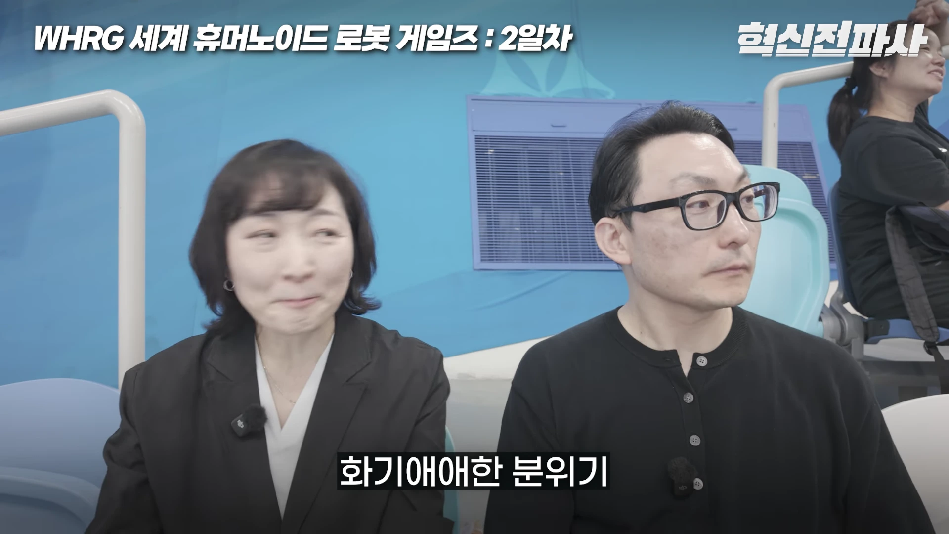 두 명의 중년 남녀가 경기장 관람석에 나란히 앉아 앞을 바라보고 있는 모습이며 화면 상단에는 행사 제목이, 하단에는 화기애애한 분위기라는 자막이 표시되어 있습니다.