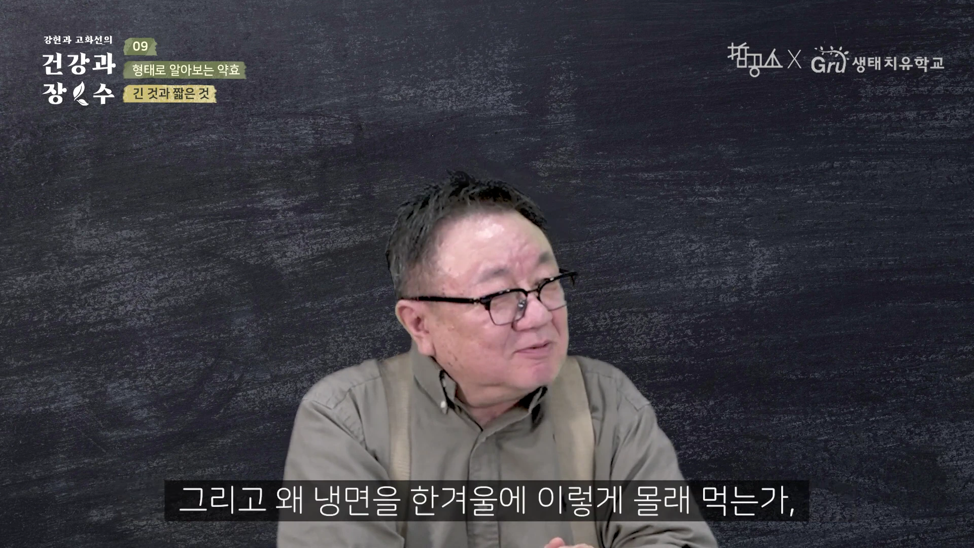 검은색 배경 앞에 안경을 쓴 중년 남성이 앉아 이야기를 나누고 있는 영상 화면.