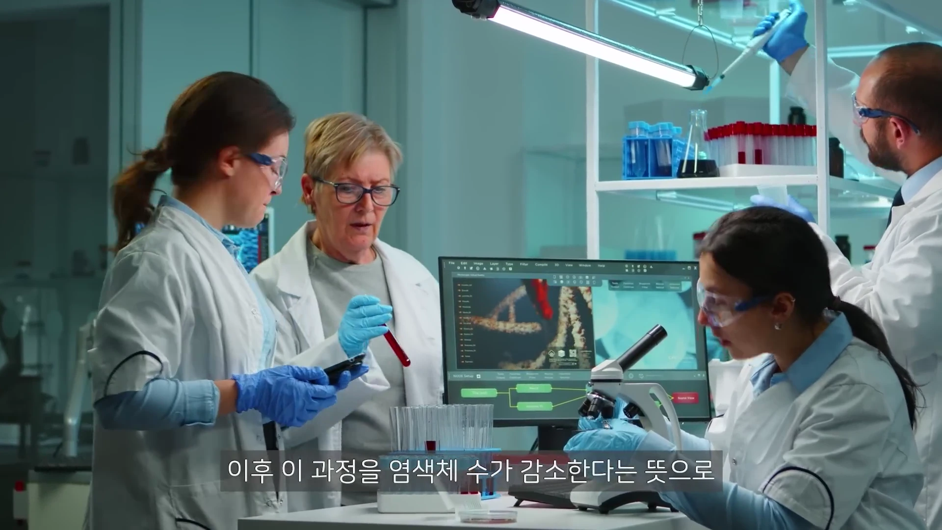 실험실에서 흰 가운을 입은 연구원들이 현미경과 모니터 화면을 보며 세포 연구를 진행하고 있는 모습