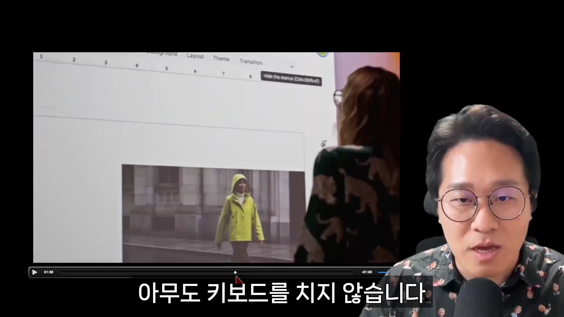 안경을 쓴 남성이 마이크 앞에서 발표하고 있으며, 그 옆으로 프레젠테이션 프로그램 화면을 조작하는 사람의 모습이 담긴 영상이 재생되고 있습니다.