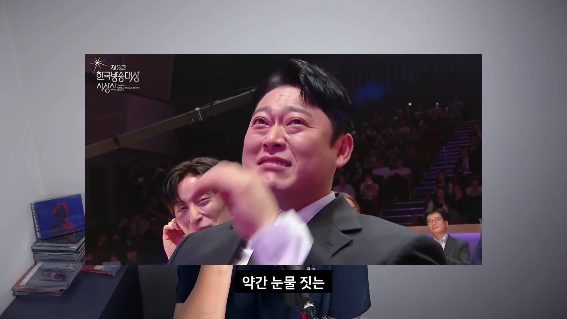 시상식 객석에 앉아 감정이 북받친 듯 눈물을 글썽이는 남성의 얼굴이 담긴 방송 화면