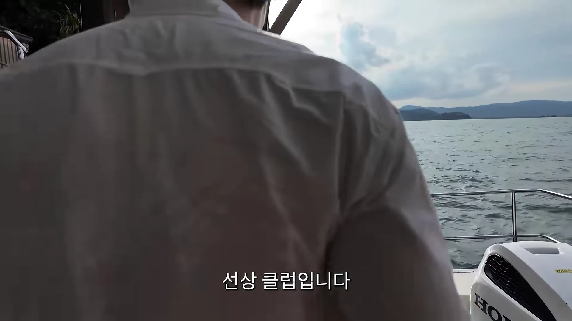 흰 셔츠를 입은 남성이 배의 갑판에서 바다를 바라보고 있는 모습이 담긴 영상 캡처 화면이며, 화면 하단에는 선상 클럽입니다라는 자막이 적혀 있다.