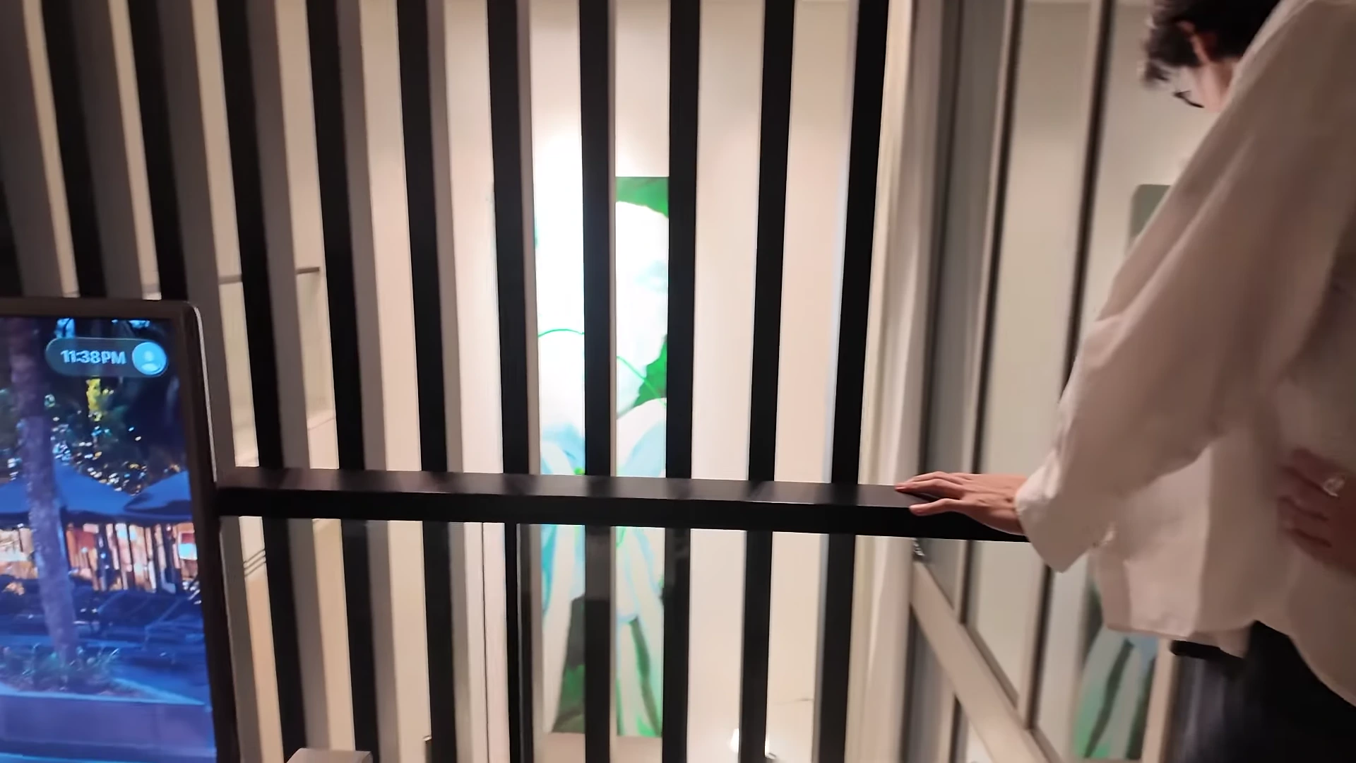 흰색 셔츠를 입은 남성이 복층 구조 숙소의 난간에 기대어 아래층을 내려다보고 있는 실내 모습입니다.