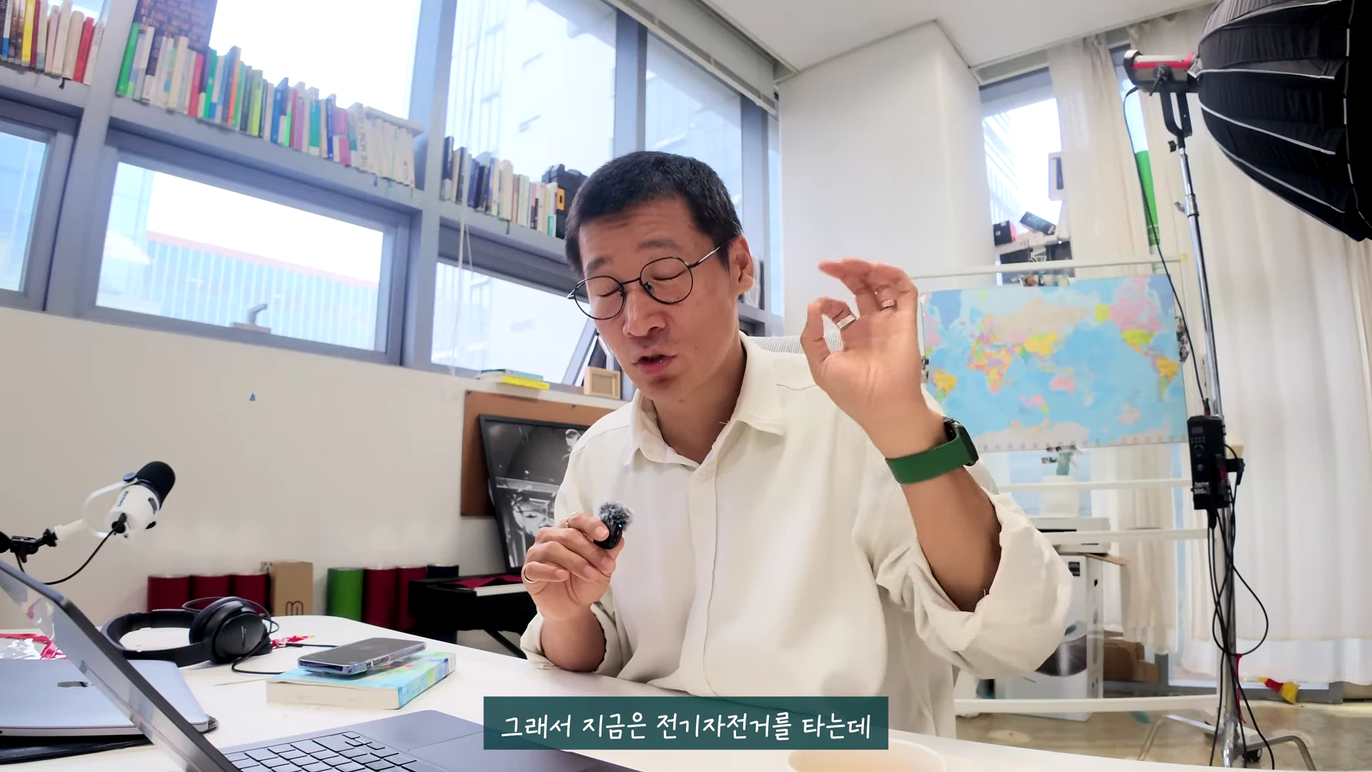 안경을 쓴 남성이 사무실 책상에 앉아 이야기하며 손으로 오케이 사인을 만들고 있고 화면 하단에는 자막이 있다.