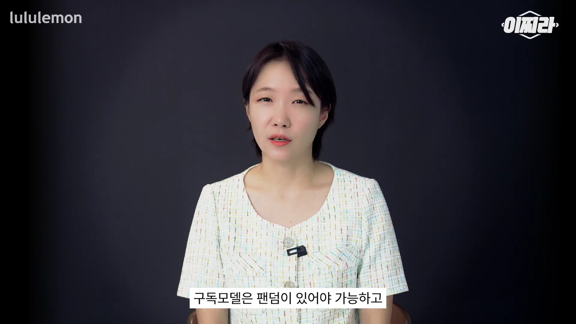 단발머리의 여성 발표자가 어두운 배경 앞에서 이야기를 하고 있는 모습.