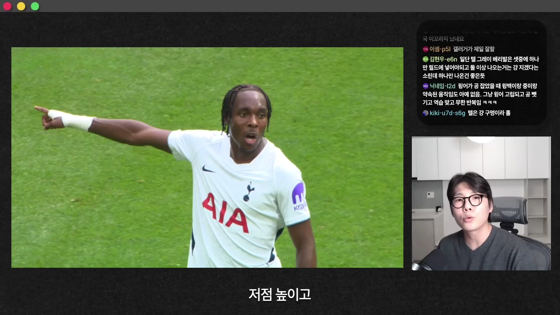 흰색 유니폼을 입은 축구 선수가 경기장에서 손가락으로 한곳을 가리키는 모습과 화면 오른쪽 아래 스튜디오에서 이야기하는 남성 출연자, 상단 채팅창이 배치된 영상 화면.