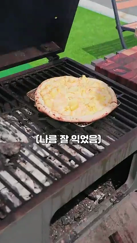 두리안 과육을 얹은 피자가 야외 그릴 위에서 노릇하게 구워지고 있는 모습이며, 화면 하단에는 '(나름 잘 익었음)'이라는 자막이 표시되어 있습니다.