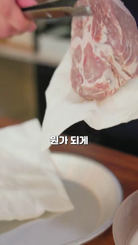 주방에서 집게를 이용해 키친타월로 돼지고기 목살의 물기를 닦아내는 모습