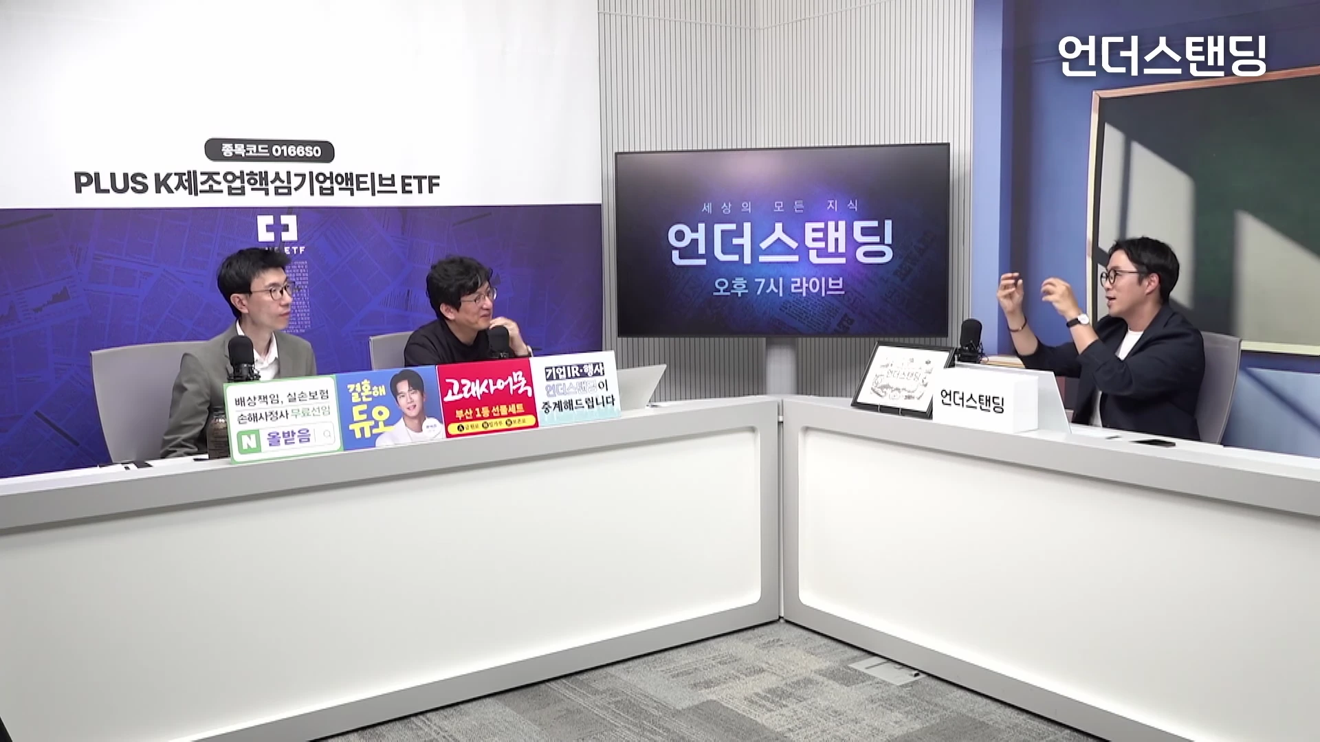 두 명의 남성과 한 명의 진행자가 스튜디오에서 대담을 나누고 있는 모습으로, 테이블 위에는 안내 문구가 놓여 있고 배경의 모니터에는 채널 로고가 표시되어 있습니다.