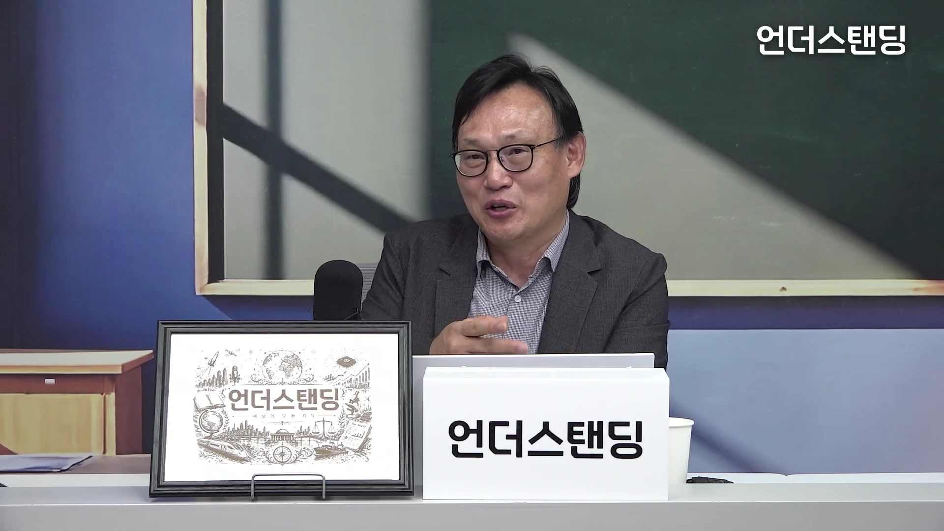 안경을 쓴 중년 남성이 스튜디오에서 마이크를 앞에 두고 이야기를 나누고 있는 모습이다.