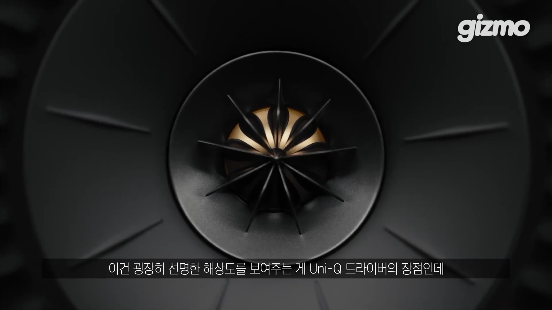 검은색 원형 구조가 중심에 배치된 동축 유니큐 드라이버의 근접 촬영 화면으로, 중앙에는 꽃 모양의 금색 부품이 있고 하단에는 자막이 포함되어 있습니다.