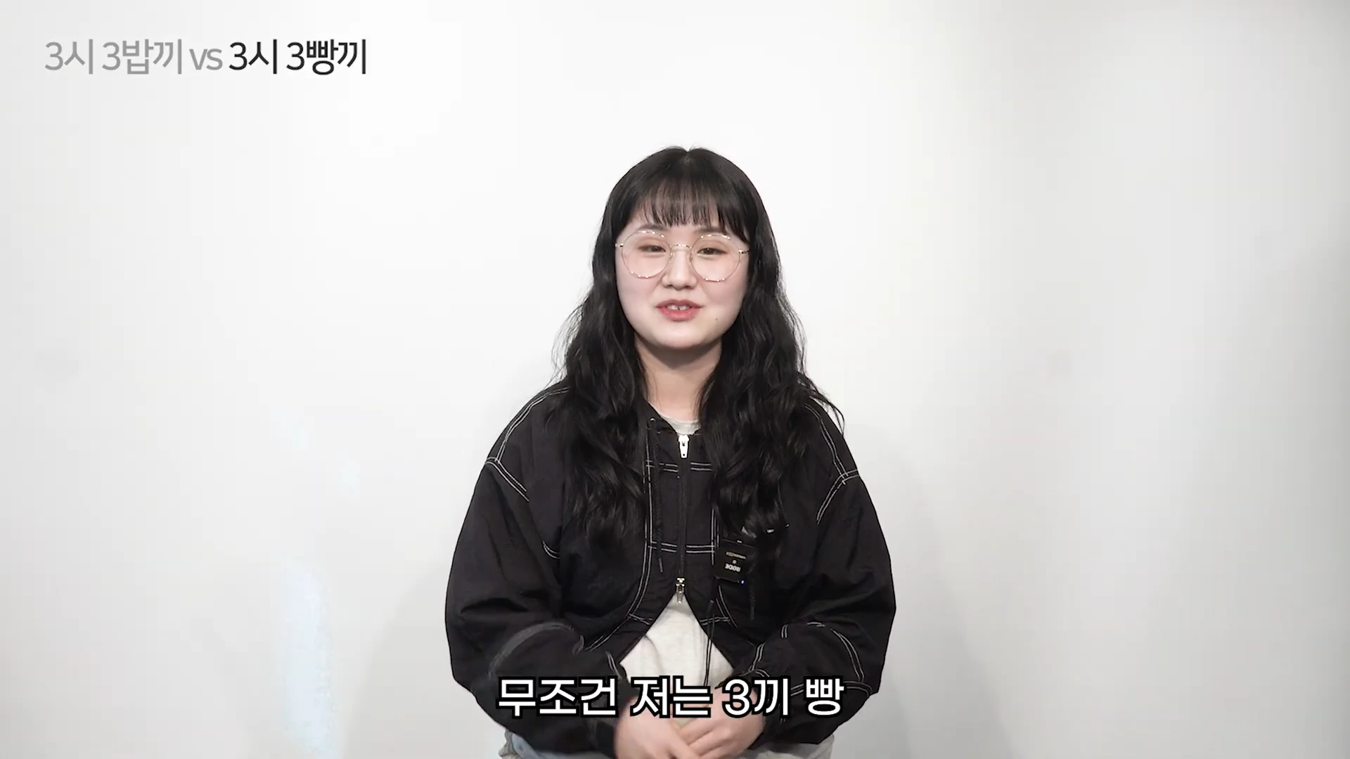 흰색 배경 앞에 안경을 쓰고 검은색 아우터를 입은 여성이 앉아 인터뷰를 하는 모습이 담긴 영상 캡처 화면입니다. 화면 상단에는 '3시 3밥끼 vs 3시 3빵끼'라는 텍스트가 있고, 하단에는 '무조건 저는 3끼 빵'이라는 자막이 적혀 있습니다.