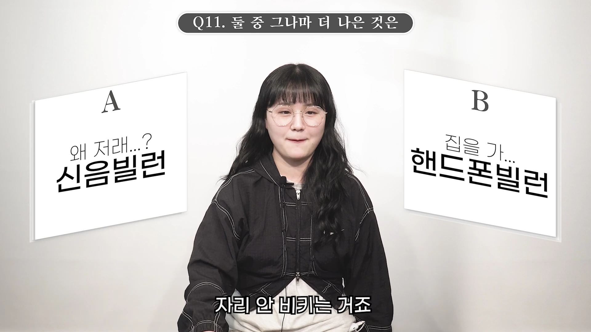 안경을 쓴 여성이 흰색 배경 앞에 앉아 있으며, 양옆으로 'A 신음빌런'과 'B 핸드폰빌런'이라는 선택지가 적힌 그래픽이 떠 있다.