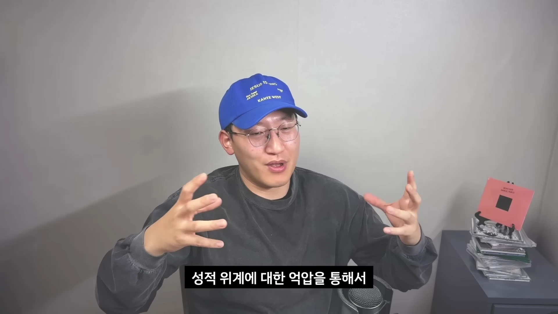 푸른색 야구 모자를 쓴 남성이 안경을 쓰고 두 손을 들어 올리며 이야기를 하고 있으며, 화면 하단에는 '성적 위계에 대한 억압을 통해서'라는 한글 자막이 표시되어 있습니다.