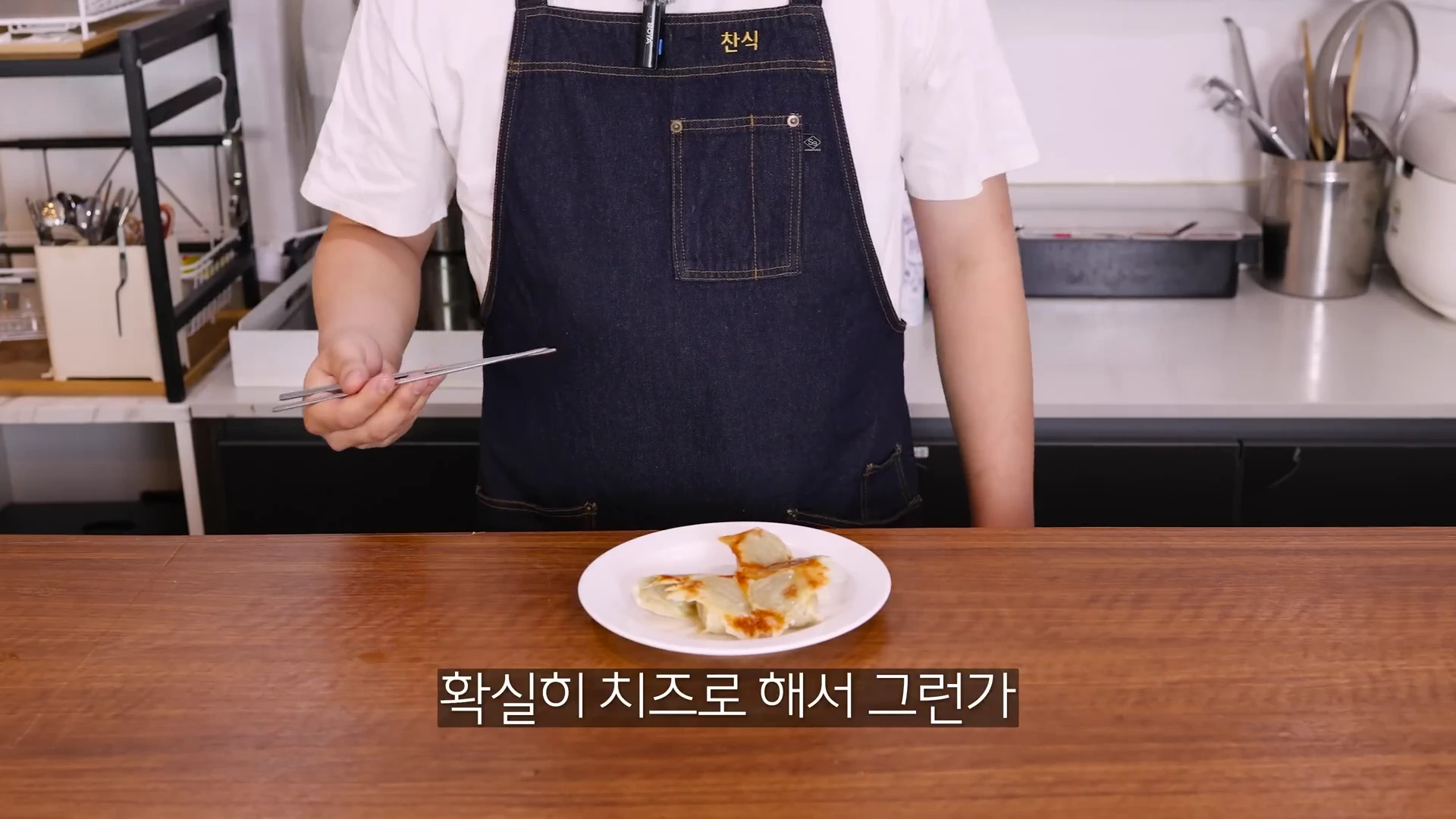 앞치마를 입은 요리사가 젓가락을 들고 완성된 치즈 눈꽃 만두가 담긴 접시를 보여주고 있습니다.