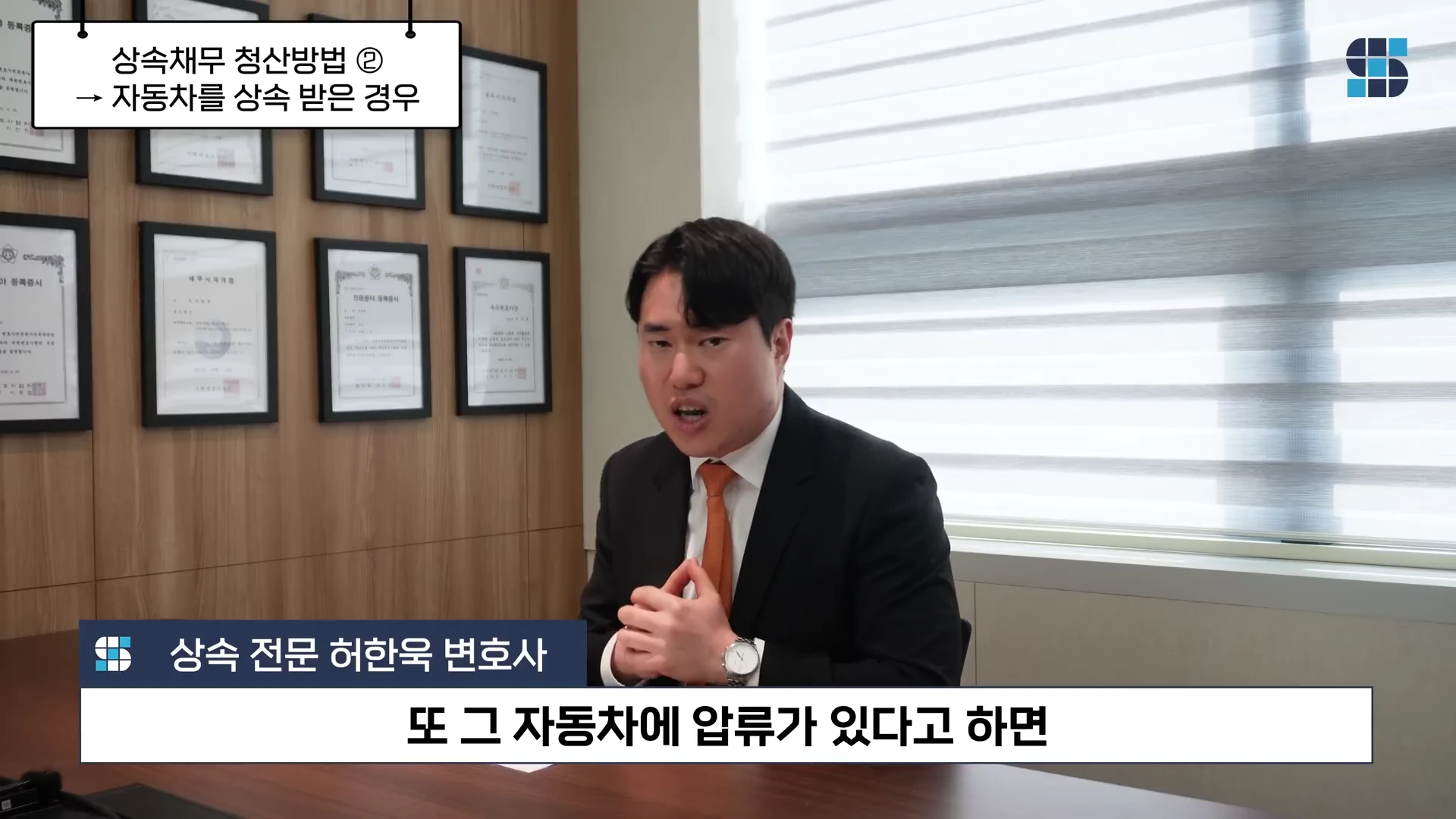 정장을 입은 변호사가 사무실 책상 앞에 앉아 이야기하고 있으며, 화면 상단에는 '상속채무 청산방법 2, 자동차를 상속받은 경우'라는 자막과 하단에는 '또 그 자동차에 압류가 있다고 하면'이라는 자막이 표시되어 있습니다.