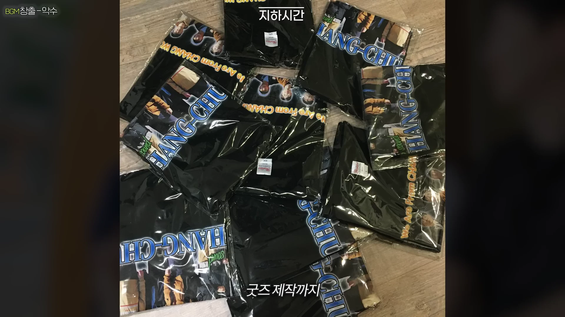비닐에 포장된 여러 개의 검은색 밴드 굿즈 티셔츠가 바닥에 어지럽게 놓여 있는 모습이다.