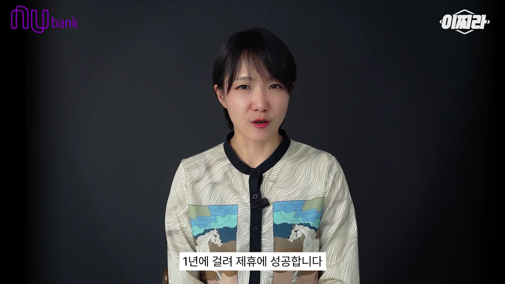 검은색 배경의 스튜디오에서 중단발의 여성이 카메라를 정면으로 응시하며 이야기하고 있고, 화면 하단에는 '1년에 걸려 제휴에 성공합니다'라는 자막이 표시되어 있습니다.