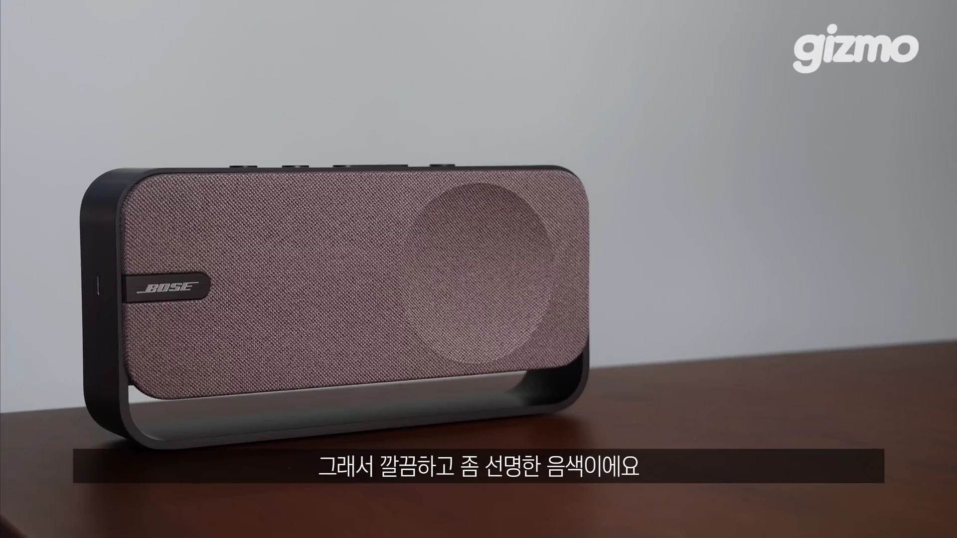 테이블 위에 놓인 보스 브랜드의 패브릭 소재가 돋보이는 사각형 디자인의 휴대용 스피커.