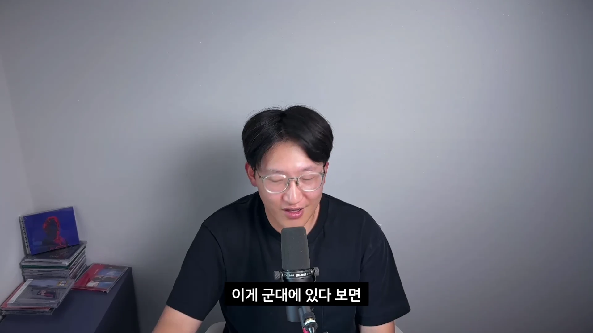 검은색 티셔츠를 입고 안경을 쓴 남성이 마이크 앞에 앉아 이야기를 하고 있으며 화면 하단에 자막이 표시되어 있다.