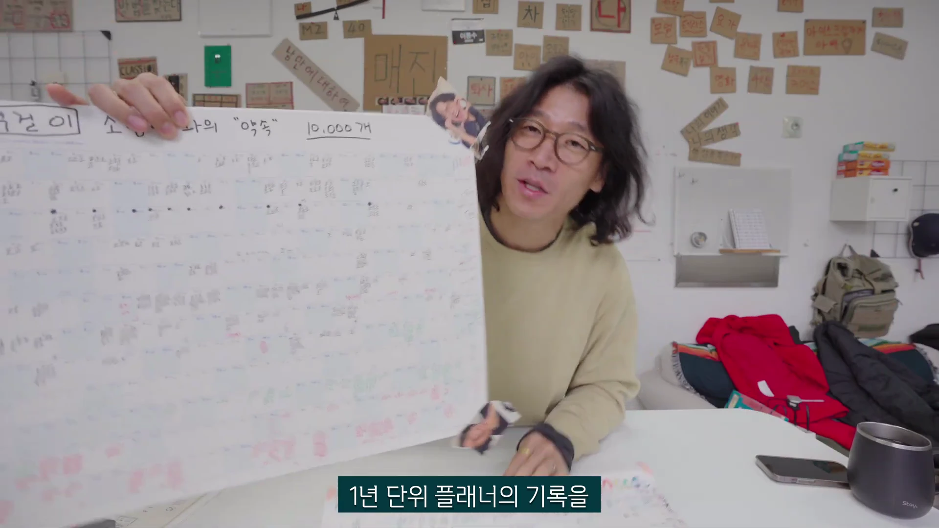 안경을 쓴 남성이 '턱걸이 1만 개와의 약속'이라고 적힌 대형 연간 기록지를 양손으로 펼쳐 보여주고 있다.