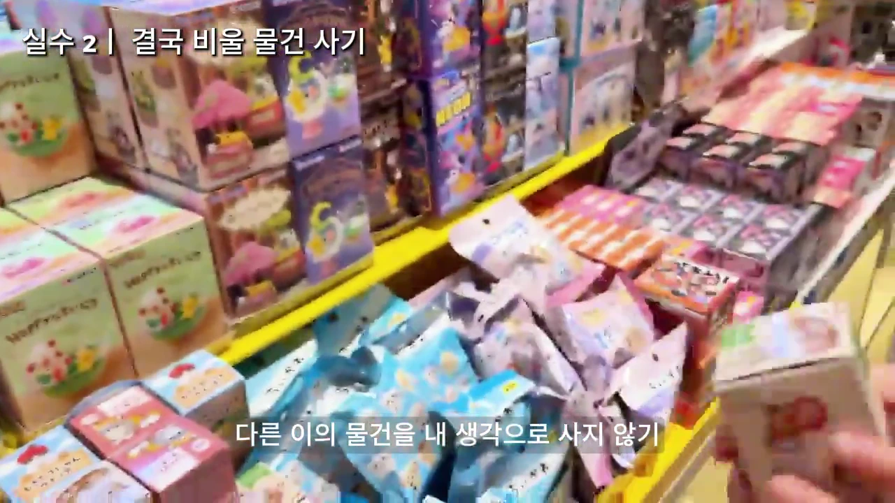 매장 진열대에 여러 종류의 장난감 상자들이 빼곡하게 놓여 있고, 한 손이 그중 작은 상자 하나를 집어 들고 있는 모습.