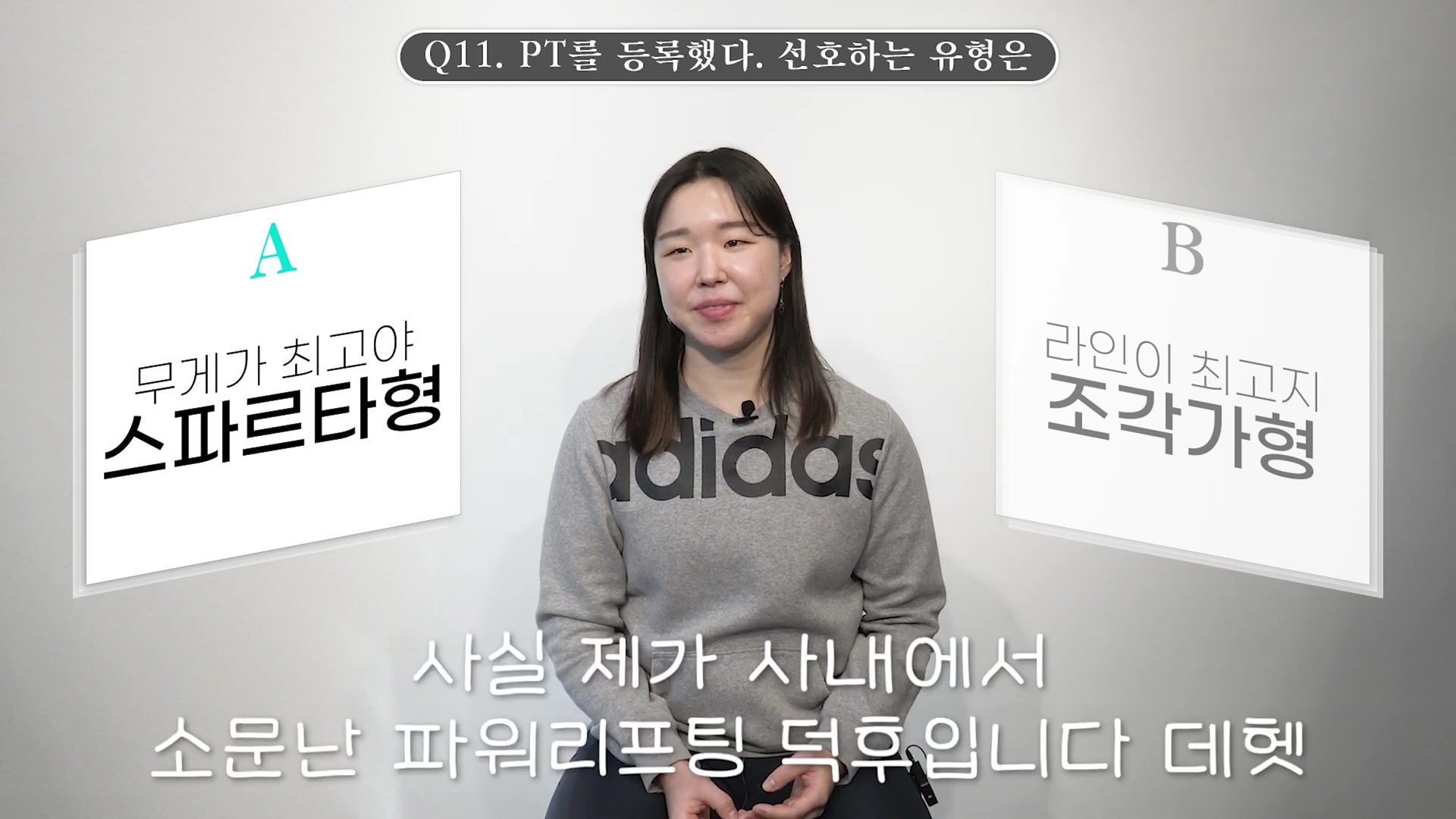 A woman wearing a gray sweatshirt sits in front of a white background while participating in a balance game with two options displayed on screen: 'A. Spartan type who values weight' and 'B. Sculpting type who values lines'.