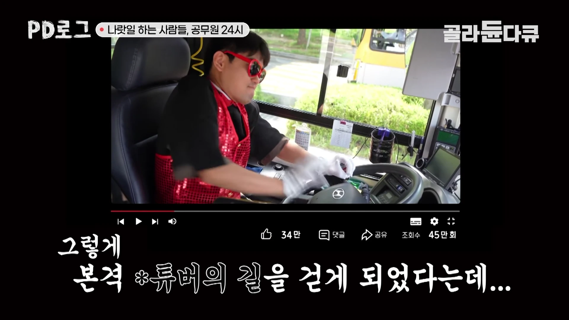 붉은색 반짝이는 조끼와 선글라스를 착용한 남성이 버스 운전석에 앉아 운전대를 잡고 있는 모습이 담긴 영상 캡처 화면입니다.
