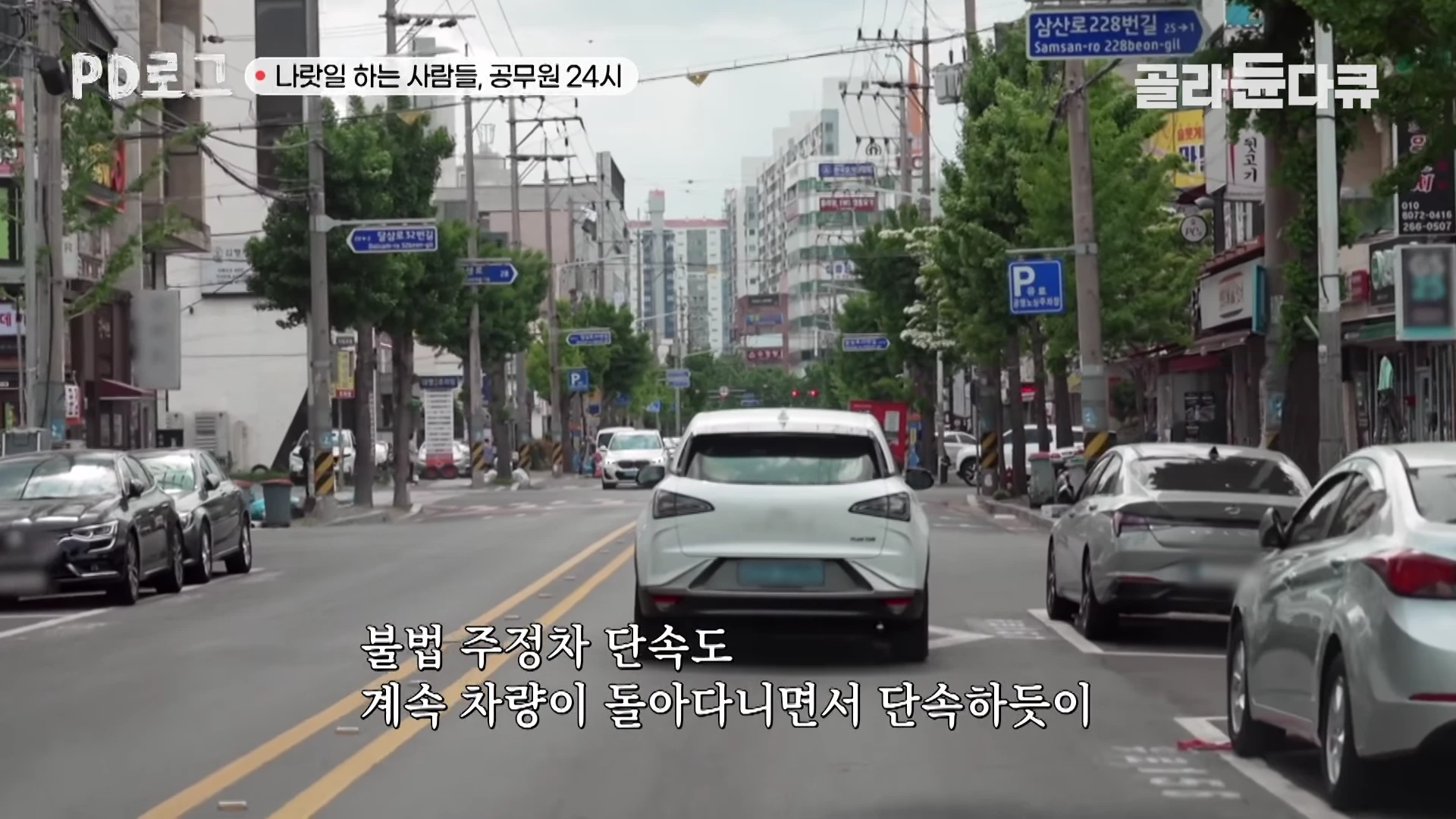도로 위에서 단속 차량이 앞서가는 흰색 승용차를 뒤따라가는 장면이 담긴 영상 캡처 화면이며, 상단에는 프로그램 로고와 제목이 적혀 있고 하단에는 불법 주정차 단속에 관한 자막이 표시되어 있습니다.