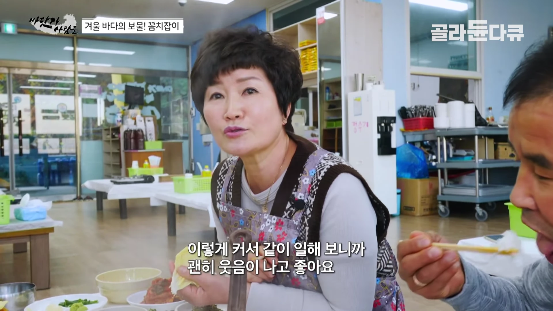 식당 안에서 한 여성이 꽃무늬 앞치마를 두르고 젓가락으로 음식을 먹으며 대화하는 모습이 담긴 방송 화면이며, 화면 하단에는 '이렇게 커서 같이 일해 보니까 괜히 웃음이 나고 좋아요'라는 자막이 표시되어 있다.