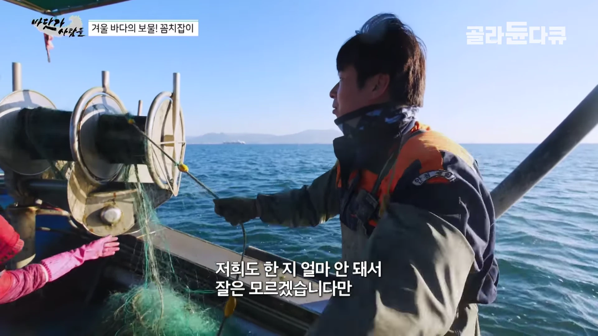 배 위에서 작업복을 입은 어부가 그물을 올리고 있으며, 화면 하단에는 자막이 겹쳐져 있습니다.