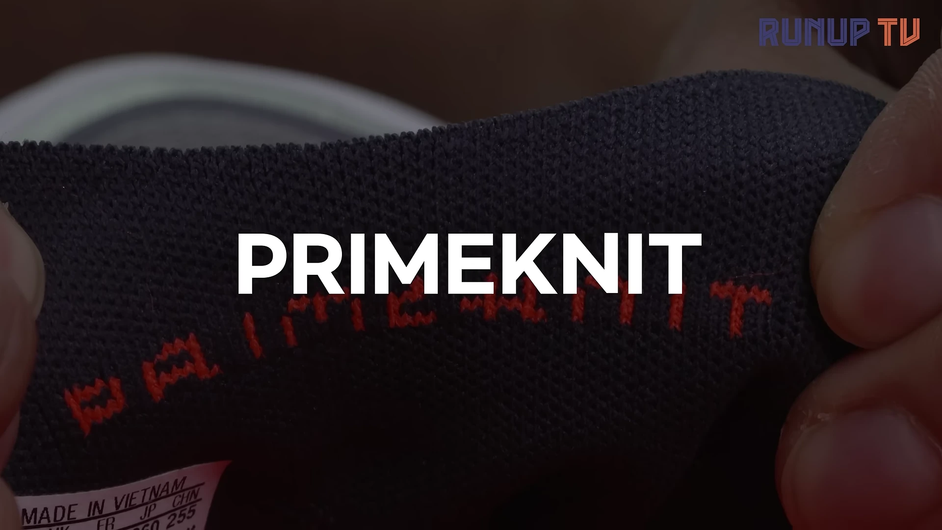 러닝화의 설포 안쪽에 자수로 새겨진 PRIMEKNIT 로고가 손가락에 잡혀 있는 근접 촬영 화면
