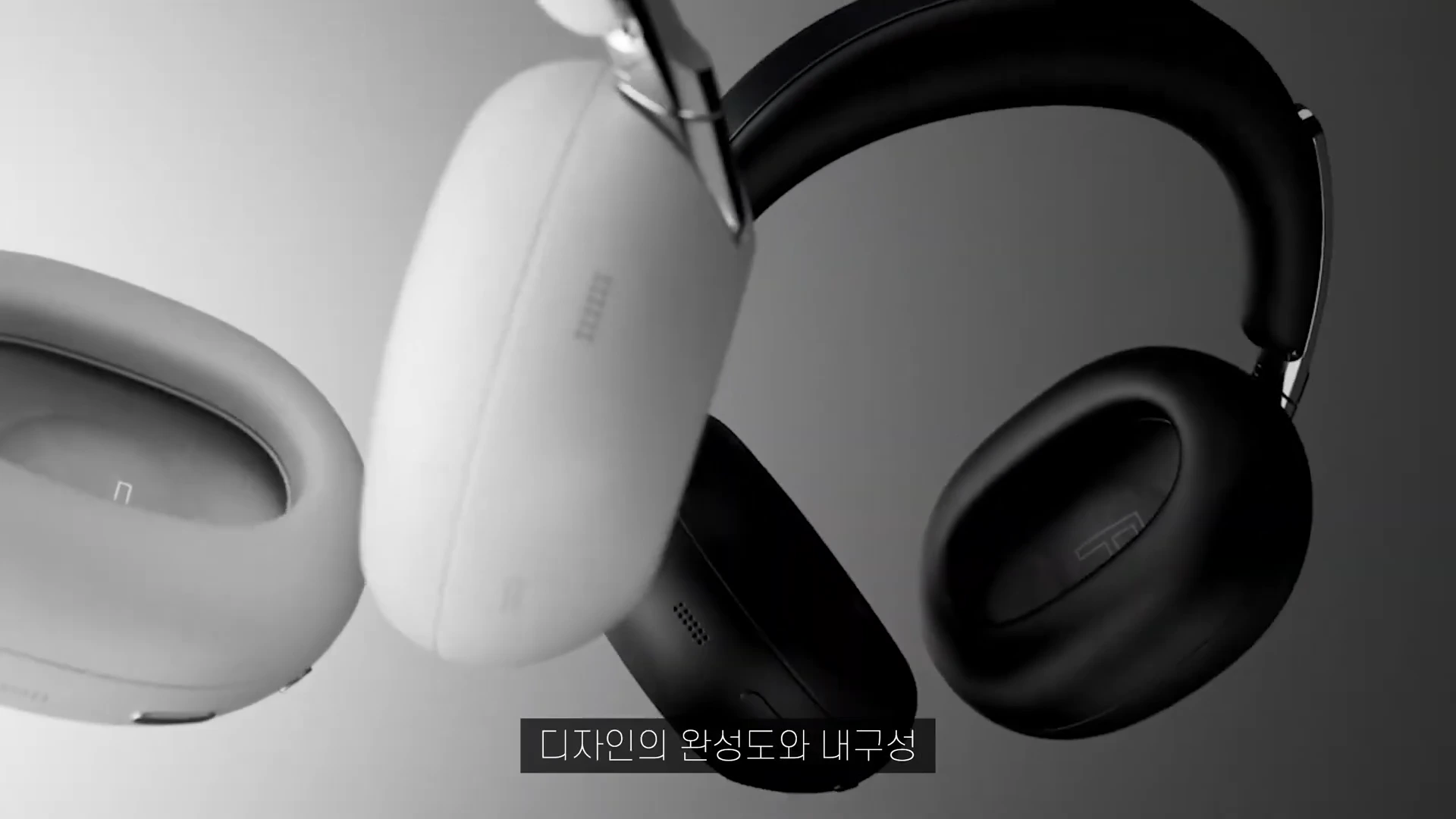 흰색과 검은색 무선 헤드폰 두 개가 공중에 떠 있는 모습과 함께 하단에 '디자인의 완성도와 내구성'이라는 자막이 표시된 영상 화면.