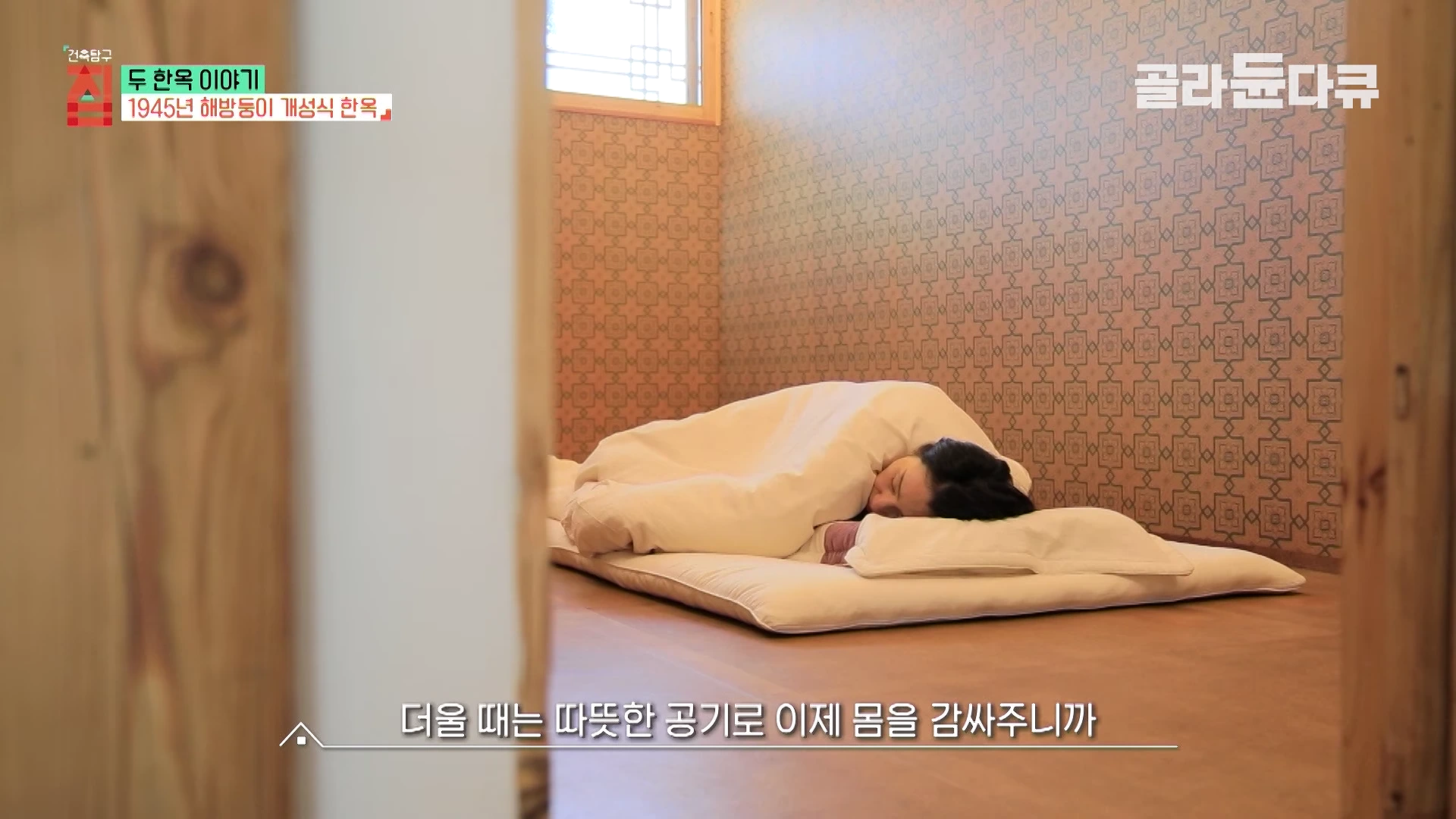 한 여성 한옥의 방 안에서 이불을 덮고 단잠을 자고 있는 모습, 벽면에는 패턴 벽지가 붙어 있다.